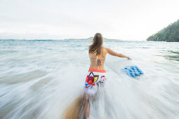 Young female surfer running into the sea, Sao Tome, Sao Tome and Príncipe, Africa