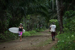 Young female surfer walking on a path through a forest, Sao Tome, Sao Tome and Principe, Africa