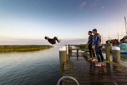 Three young people have fun and jump with a backflip from a pier in the Bodden by Ahrenshoop. Ahrenshoop, Althagen, Darß, Mecklenburg-Vorpommern, Germany