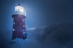 Young male skier standing at a lighthouse during a snowstorm at night, Andermatt, Uri, Switzerland