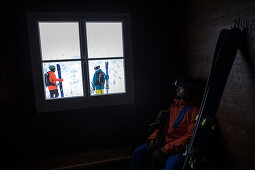 Junger Skifahrer betrachtet andere Skifahrer durch ein Fenster, Andermatt, Uri, Schweiz