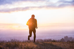 Young man running over a meadow during sunset, Allgaeu, Bavaria, Germany