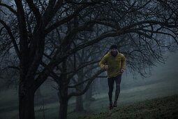 Young man running over a meadow between trees on a foggy autumn day, Allgaeu, Bavaria, Germany