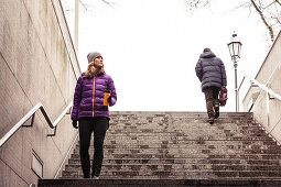 Young woman with coffee mug descents the subway stairs on Königs Plaza in Munich, Bavaria, Germany