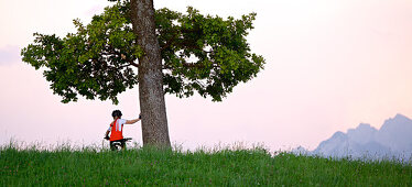 girl sitting on her bike and holding on to a tree, Fuessen, Bavaria, Germany