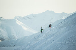 Zwei junge Skifahrer laufen durch den Tiefschnee auf den Gipfel eines Berges, Gudauri, Mzcheta-Mtianeti, Georgien