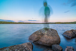 Kind steht auf einem Stein im See  im Abendlicht wie ein Schemen, See nähe Munkfors, Värmland, Schweden