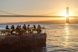 sunset on riverfront restaurant Ponto Final, view from south bank of River Tagus,and the 25th April Bridge, Cacilhas, Almada, Lisbon, Portugal