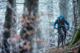 Young man riding with his bike through a with frost covered forest, Allgaeu, Bavaria, Germany