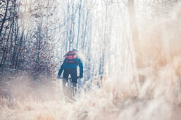 Young man riding with his bike through a with frost covered forest, Allgaeu, Bavaria, Germany