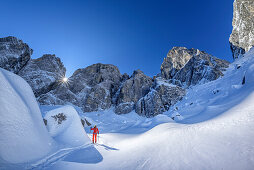 Woman backcountry skiing ascending towards Sella Nabois, Jof Fuart and Sella Nabois in background, Julian Alps, Friaul, Italy