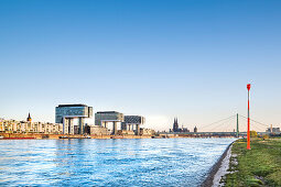 View over river Rhein towards Rheinau harbour with crane houses, Cologne Cathedral, Cologne, North Rhine-Westphalia, Germany