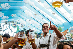 Junger Man in Lederhosen auf den Bierbänken feiern Oktoberfest im Bierzelt