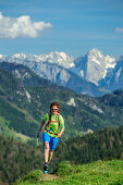 Woman trail running crossing ridge, Kaiser range in background, Mitterberg, Bavarian Alps, Upper Bavaria, Bavaria, Germany