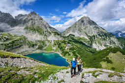 Man and woman hiking ascending towards Hinterer Tajakopf, lake Drachensee, Drachenkopf and Ehrwalder Sonnenspitze in background, Hinterer Tajakopf, Mieming Mountains, Tyrol, Austria