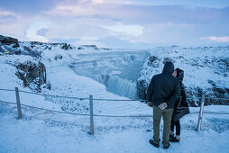 Junges Paar blickt über den Gullfoss (gull = Gold, foss = Wasserfall) Wasserfall am Fluss Hvítá (Hvita) im verschneiten Winter, Island, Iceland, Europa