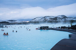 People bathe and swim at The Blue Lagoon, the famous wellness thermal pool with its typical blue-white water in winter time, near Grindavik, Reykjanes, Iceland, Europe