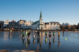 School children play soccer on frozen Tjörnin lake with Fríkirkjan (Frikirkjan) church behind, Reykjavik, Iceland, Europe