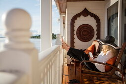 Junge Frau entspannt sich auf Balkon der Executive Suite an Bord Ayeyarwady (Irrawaddy) Flusskreuzfahrtschiff Anawrahta (Heritage Line), nahe Kyunttaw, Kachin, Myanmar