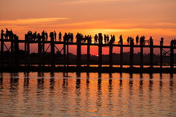 Silhouette of people walking along U Bein Bridge across Taungthaman Lake at sunset, Amarapura, Mandalay, Myanmar