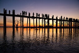 Silhouette of people walking along U Bein Bridge across Taungthaman Lake at sunset, Amarapura, Mandalay, Myanmar