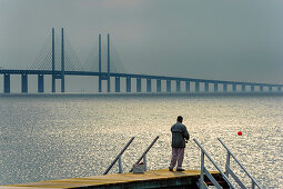 Gewitterstimmung über der Öresundbrücke und Sonne strahlt auf das Meer, Mann angel auf einem Bootssteg, Oresundbrücke, Malmö, Südschweden, Schweden