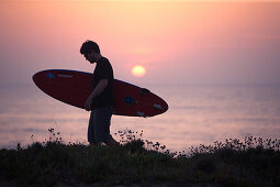Junger Surfer läuft mit seinem Brett am Strand von Praia da Amoreira,  Aljezur, Faro, Portugal