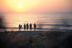 Fünf junge Surfer stehen am Strand von Praia da Amoreira bei Sonnenuntergang,  Aljezur, Faro, Portugal