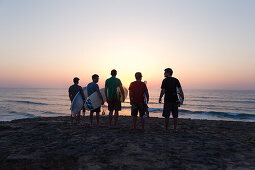 Fünf junge Surfer stehen am Strand von Praia da Amoreira bei Sonnenuntergang,  Aljezur, Faro, Portugal