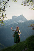 Young woman in traditional costume taking a selfie with her mobile on Falkenstein in Allgaeu, Pfronten, Bavaria, Germany