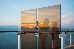 Paar fotografiert Sonnenuntergang von hinter Windschutz Fenster auf Deck 14 an Bord von Kreuzfahrtschiff Mein Schiff 6 (TUI Cruises), Ostsee, nahe Dänemark, Europa