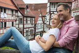 Couple relaxes on city wall with half-timbered houses in Altstadt old town behind, Bad Orb, Spessart-Mainland, Hesse, Germany