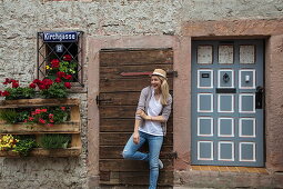 Beautiful blond woman with sun hat poses in front of wall in Altstadt old town, Bad Orb, Spessart-Mainland, Hesse, Germany