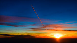 Der Kondensstreifen eines höher fliegenden Flugzeugs wird orange angestrahlt, Sonnenuntergang aus dem Cockpit über Frankreich