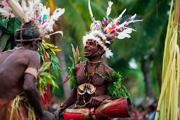 A man wearing traditional garb and headdress smiles while holding a drum during a cultural performance, Kopar, East Sepik, Papua New Guinea, South Pacific
