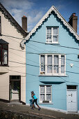 blau gekleidetet Frau vor blauem Deck of Cards Haus (bunte steile Häuser in West View Straße), Cobh, Grafschaft Cork, Irland, Europa
