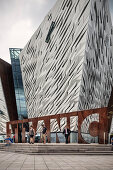man in suit walks through TITANIC capital letters, modern architecture of Titanic Exhibition Centre, Belfast, Northern Ireland, United Kingdom, Europe