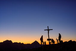 Two persons standing at dawn at cross at summit, Lagazuoi, Dolomites, UNESCO World Heritage Site Dolomites, Venetia, Italy