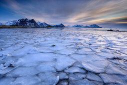 Vereiste Küste mit verschneiten Bergen im Hintergrund, Lofoten, Nordland, Norwegen