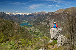 Frau beim Wandern sitzt auf Felsen und blickt auf Lago di Tenno und Adamellogruppe, Gardasee, Gardaseeberge, Trentino, Italien
