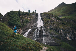 Wanderin beim Aufstieg mit Wasserfall im Hintergrund E5, Alpenüberquerung, 2. Etappe, Lechtal, Holzgau, Tirol, Österreich, Kemptner Hütte zur Memminger Hütte
