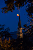 blutroter Mond auf dem Höhepunkt der Mondfinsternis 2018; im Vordergrund die Pfarrkirche St. Nikolaus in Übersee hinter einem Maisfeld