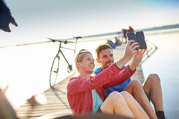 junge Frau  und junger Mann mit Fahrrädern auf Steg am Seeufer machen en Selfie, Starnberger See, Bayern, Deutschland