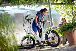 young woman fills air in a tire of an an eBike in front of an airstream trailer, Muensing, bavaria, germany