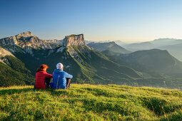 Mann und Frau sitzen auf Wiese und blicken auf Grand Veymont und Mont Aiguille im Morgenlicht, vom Tête Chevalier, Vercors, Dauphine, Dauphiné, Isère, Frankreich