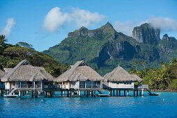 Overwater bungalows on stilts from a luxury resort are dwarfed by the high mountains in the background, Bora Bora, Society Islands, French Polynesia, South Pacific