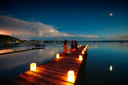 Drei Mädchen sitzen abends auf einem mit Kerzen beleuchteten Steg, Wörthsee, bayern, Deutschland