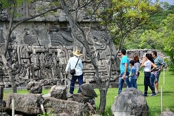 Tourists in front of a stepped temple with stone sculptures on the pre-Columbian archaeological site of Xochicalco at Cuernavaca, Mexico