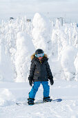 Kleiner Junge auf seinem Snowboard vor veschneiten Bäumen, Winter in Finnland