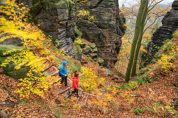 Man and woman hiking through autumn forest in the Elbe Sandstone Mountains, fire view, Elbe Sandstone Mountains, Saxon Switzerland National Park, Saxon Switzerland, Saxony, Germany